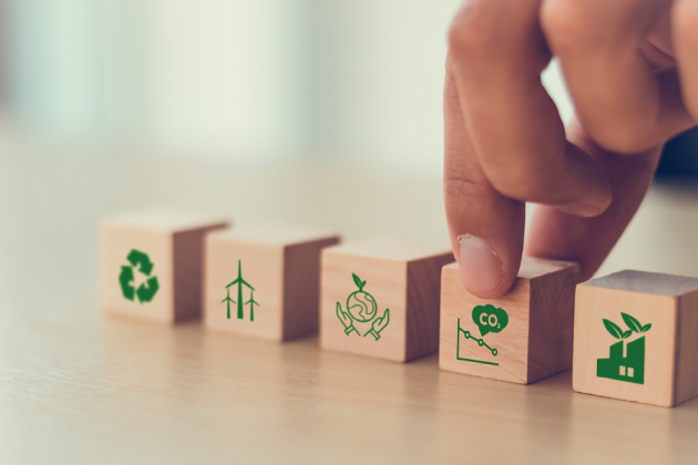 A hand arranges wooden blocks bearing recycling, renewable energy, carbon and other environmental symbols.