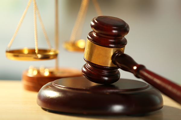 A wooden gavel rests on a sound block with brass scales behind it.