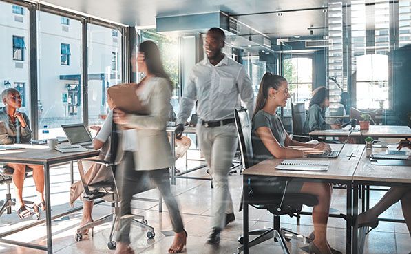 A busy, modern office with diverse professionals working at desks and others moving quickly.