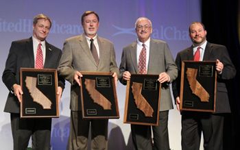 Four men in suits hold framed awards featuring California silhouettes.