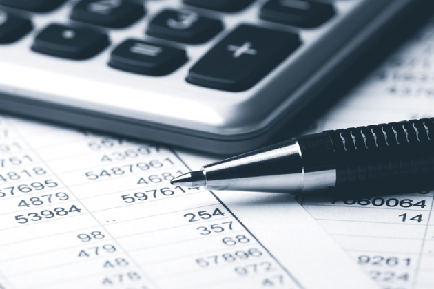 Close-up of a calculator and two pens resting on printed financial figures.