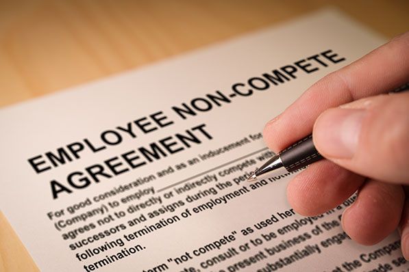 A hand holds a pen over an Employee Non-Compete Agreement.