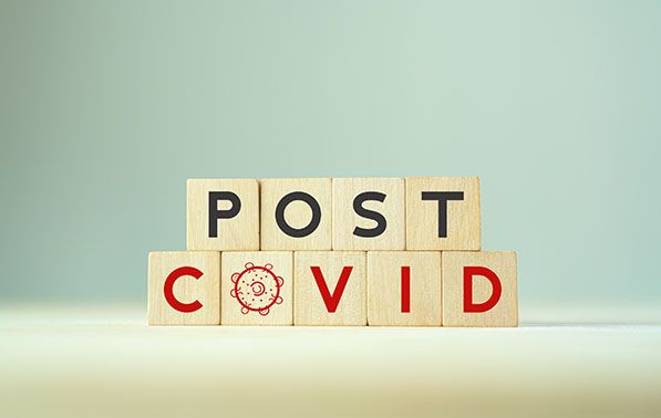 Wooden blocks spell POST COVID, with a virus symbol replacing the O in COVID.