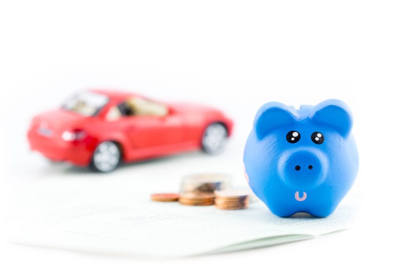 A blue piggy bank beside coins, with a red toy car in the background.