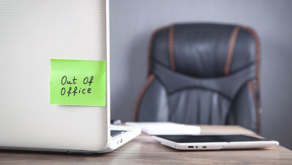 Green "Out Of Office" sticky note on a laptop in an empty office.