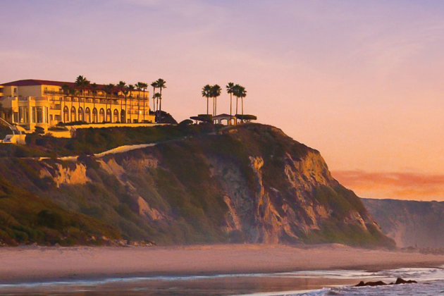 A coastal resort stands atop cliffs above a beach at sunset.