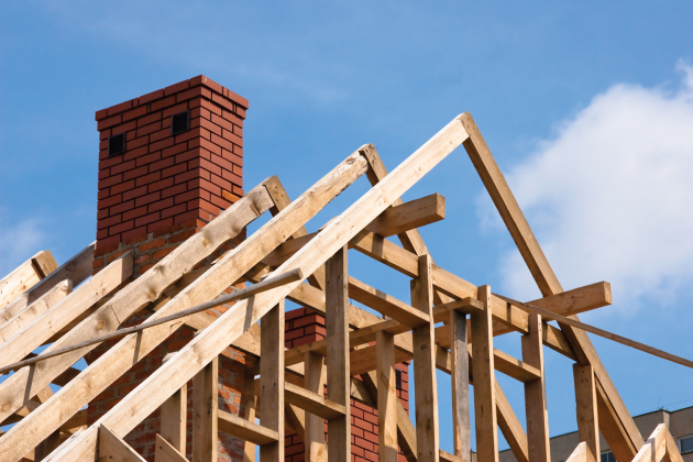 Exposed wooden roof framing and a brick chimney at a house construction site.