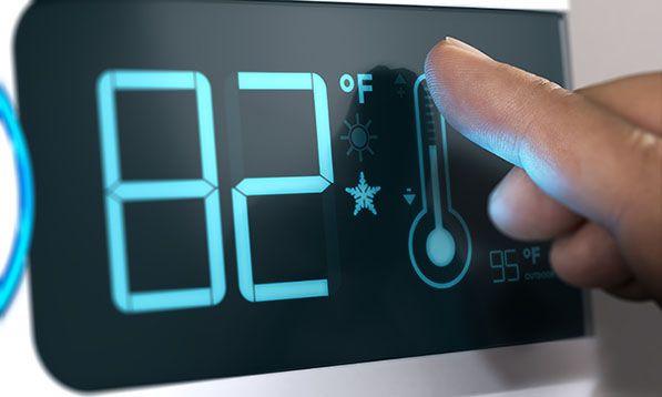 A finger adjusts a digital thermostat displaying 82 degrees Fahrenheit.
