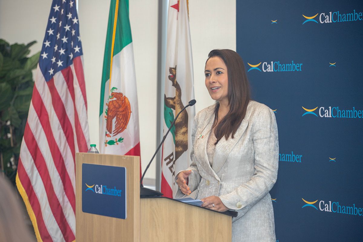 A woman speaks at a podium with US, Mexican, and California flags behind her, and CalChamber logos visible.