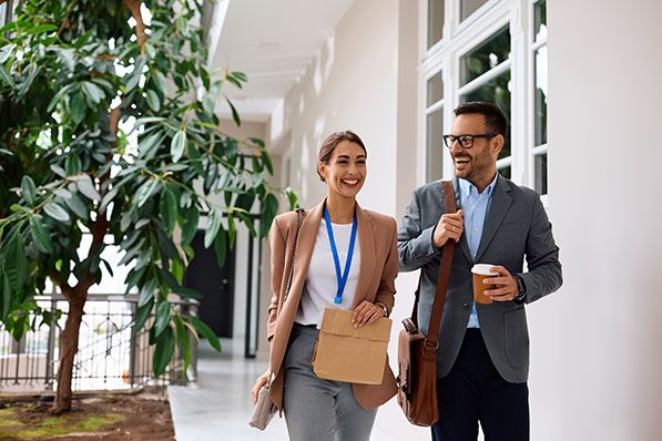 Two smiling professionals walk through a bright hallway.