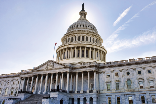 The United States Capitol dome and columned facade beneath a pale blue sky.