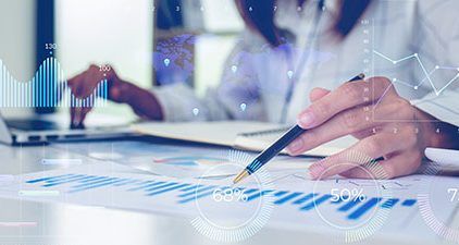 Hands use a pen and calculator over financial documents with translucent charts overlaid.