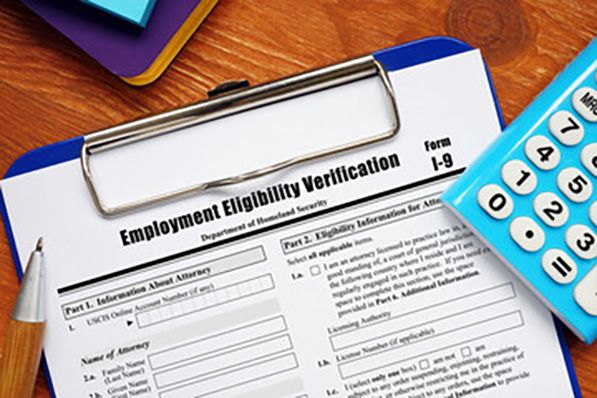 Form I-9 Employment Eligibility Verification on a clipboard with a pen and a blue calculator on a wooden desk.