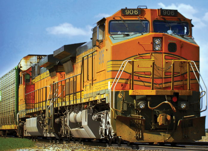 Orange and yellow freight locomotive pulls shipping containers along railroad tracks.