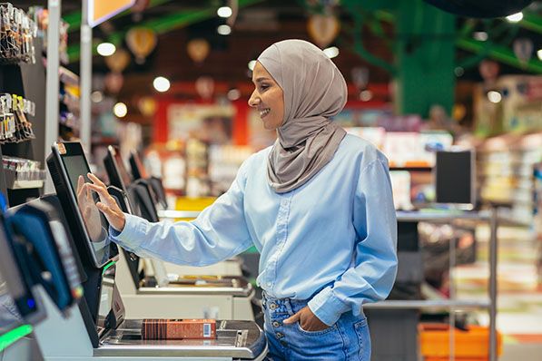 A shopper wearing a headscarf uses a supermarket self-checkout touchscreen.