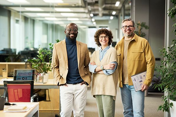 Three coworkers stand together in a plant-filled open office.
