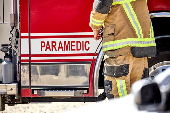 A worker in protective firefighting gear stands beside a red vehicle labeled PARAMEDIC.
