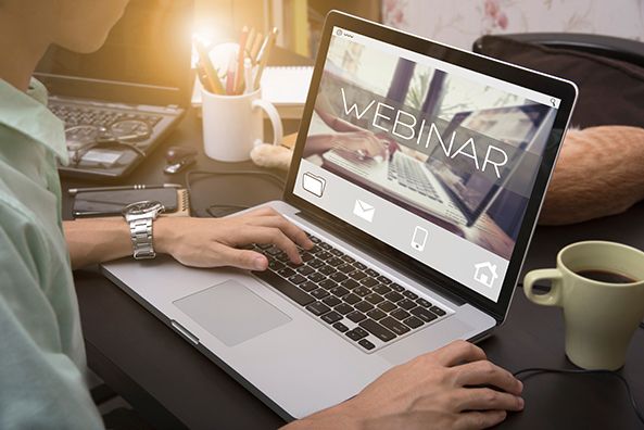 A person uses a laptop showing the word WEBINAR beside a coffee mug.