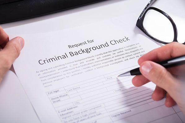 A person holds a pen over a Request for Criminal Background Check form beside glasses.