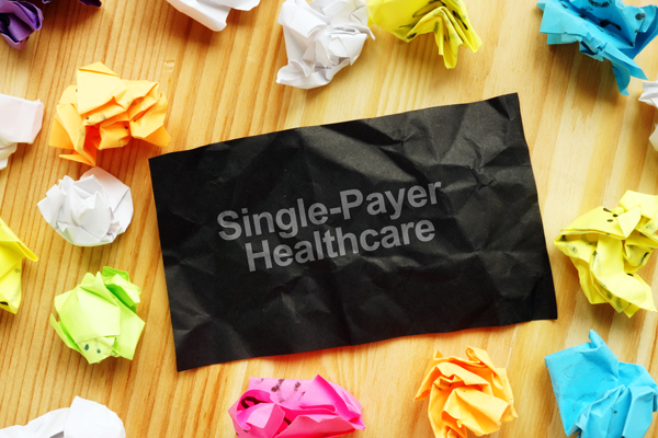 A black sheet labeled Single-Payer Healthcare lies among crumpled colorful paper on a wooden table.