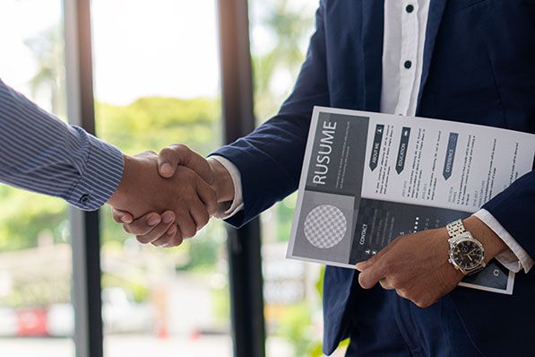 Two people shake hands while one holds a printed résumé.