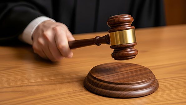 A person in a dark robe holds a wooden gavel above its block.