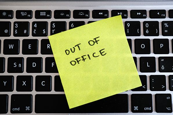 Yellow sticky note with "OUT OF OFFICE" written on it on a laptop keyboard.