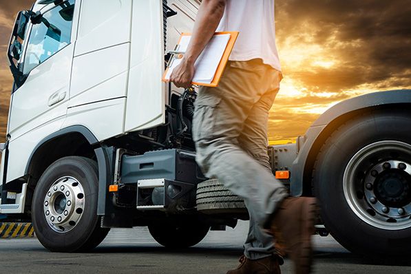 A person carrying a clipboard walks beside a white truck at sunset.