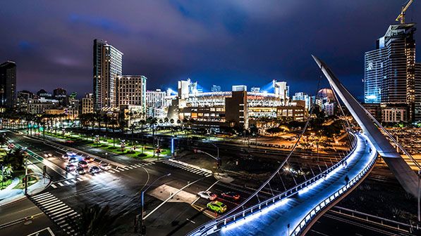 Downtown San Diego at night with an illuminated curved pedestrian bridge and city towers.