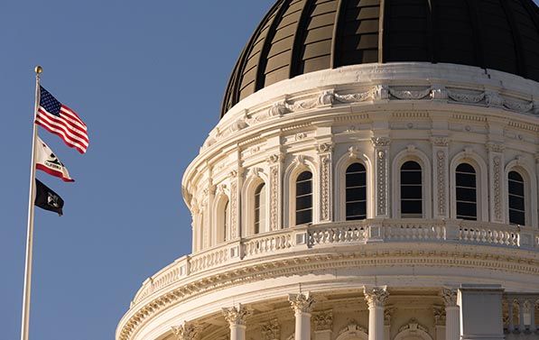 Close-up of the California State Capitol dome beside U.S. and California flags.