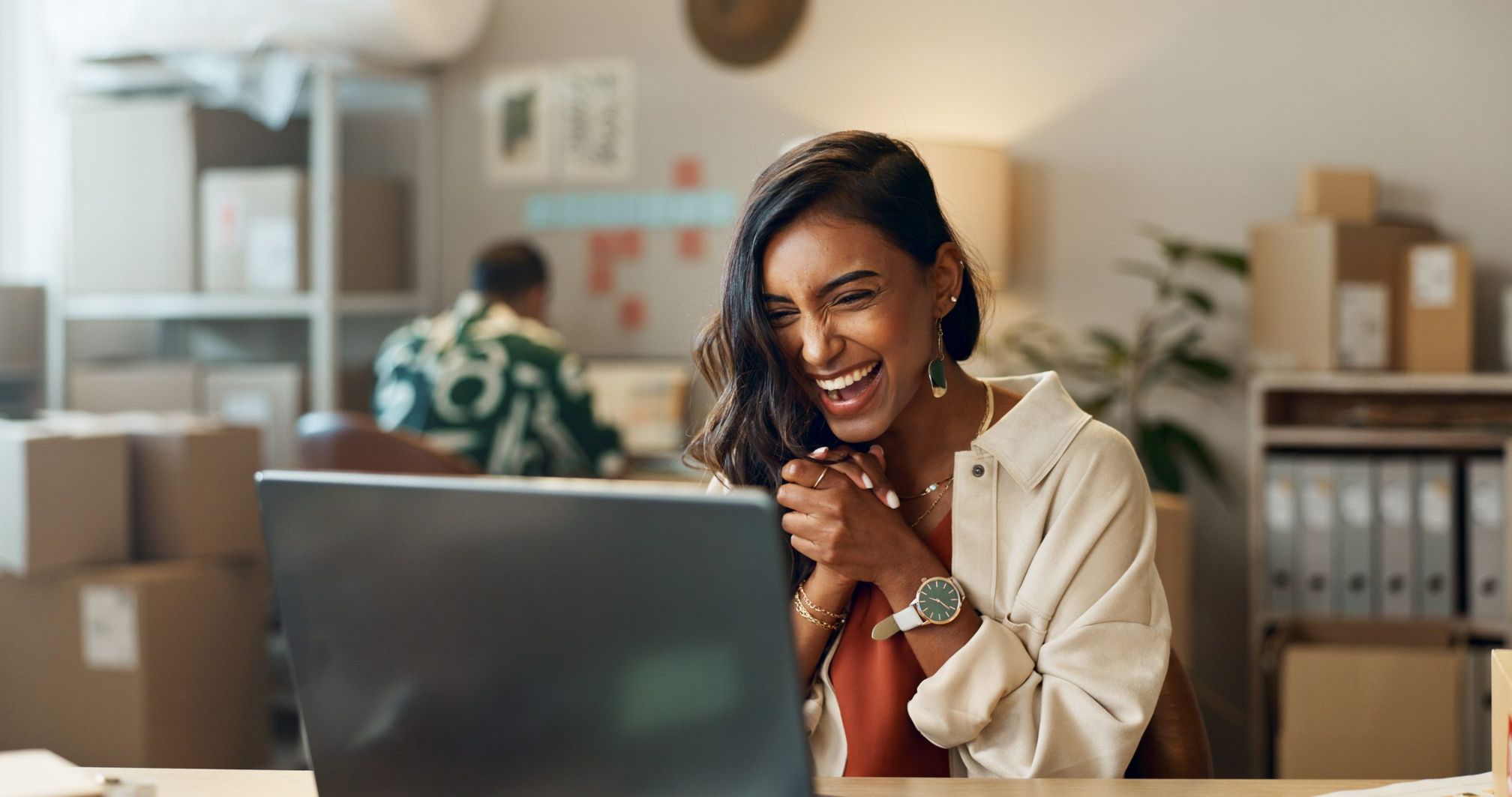 A woman smiles toward a laptop with her hands clasped in an office.