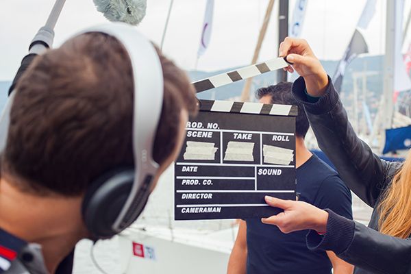 A film crew member holds a clapperboard in front of a person wearing headphones.