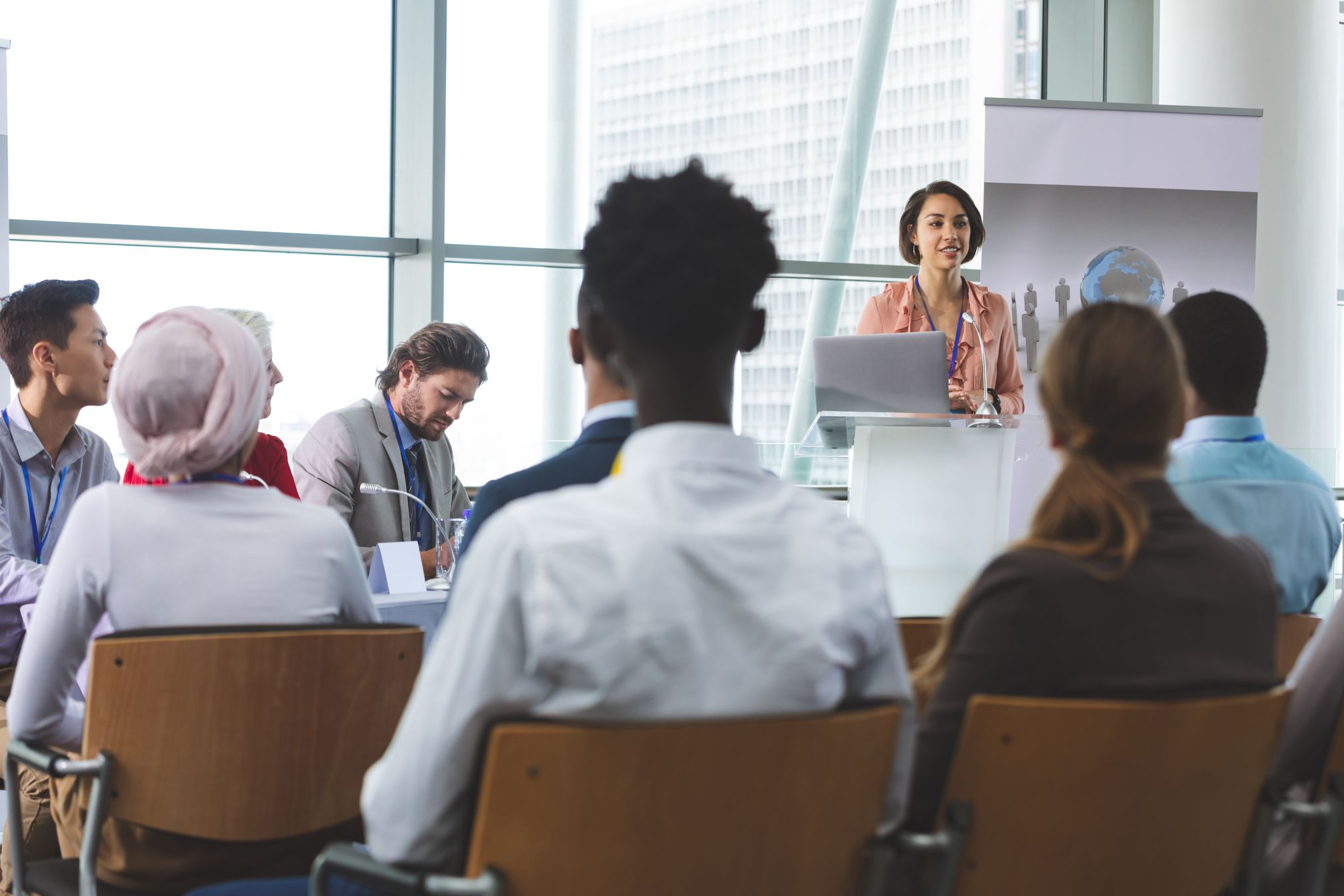 A presenter addresses seated coworkers in a bright meeting room.