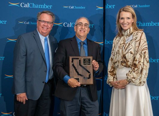 Two men and a woman pose with an award plaque before a CalChamber backdrop.