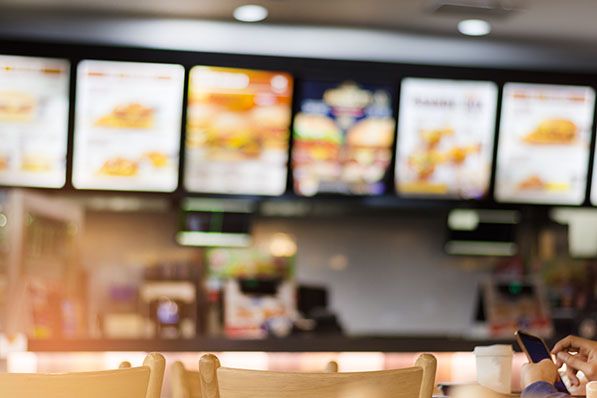 Blurred illuminated menu boards hang above a fast-food restaurant counter.