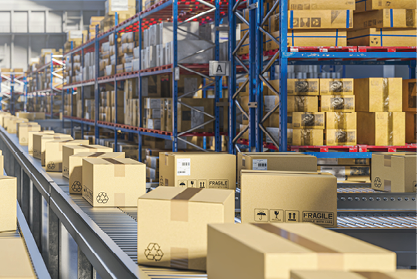 Cardboard packages travel along a conveyor beside tall warehouse storage racks.