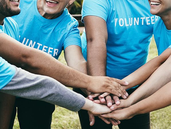 A group in blue VOLUNTEER shirts stack their hands together outdoors.