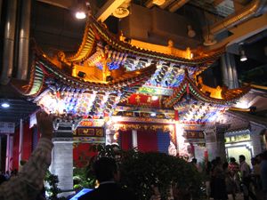 An ornate multilevel building with curved roofs illuminated in colorful lights at night.