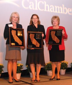 Three women stand on a stage holding framed award plaques beneath a CalChamber projection.