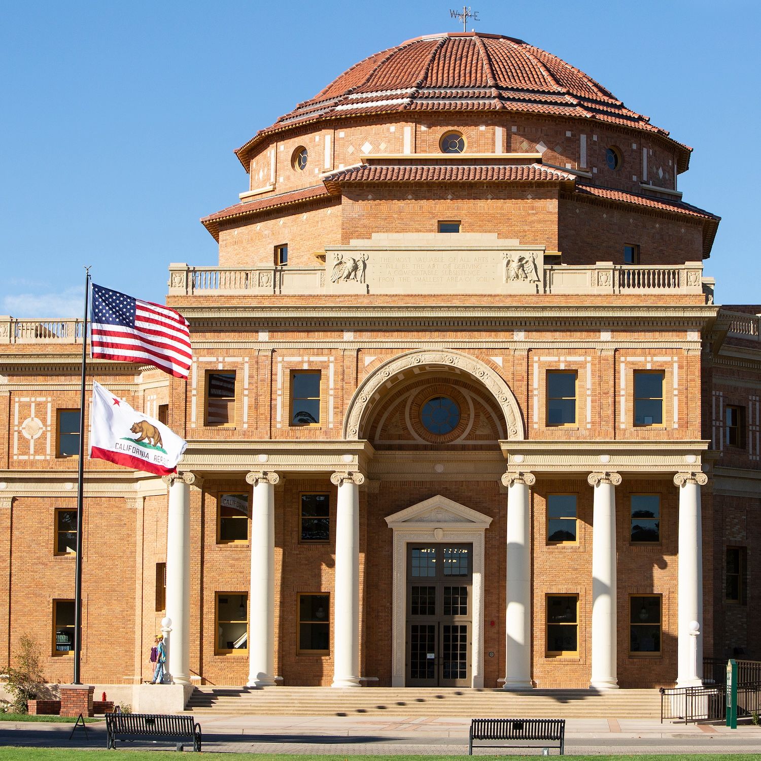 A historic brick civic building with a rounded roof, columned entrance and United States and California flags.