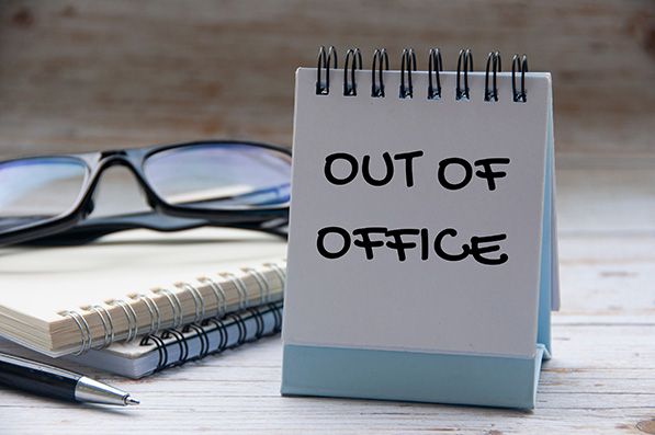 A small spiral notepad reads OUT OF OFFICE beside eyeglasses and stacked notebooks.