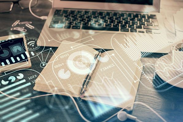A laptop, phone and notebook overlaid with translucent data charts and analytics graphics.