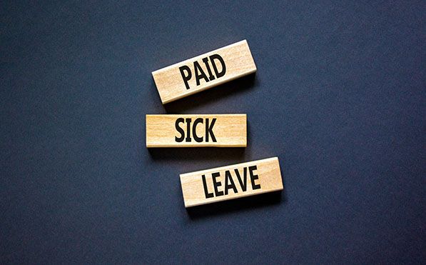 Wooden tiles spell PAID SICK LEAVE against a dark blue background.