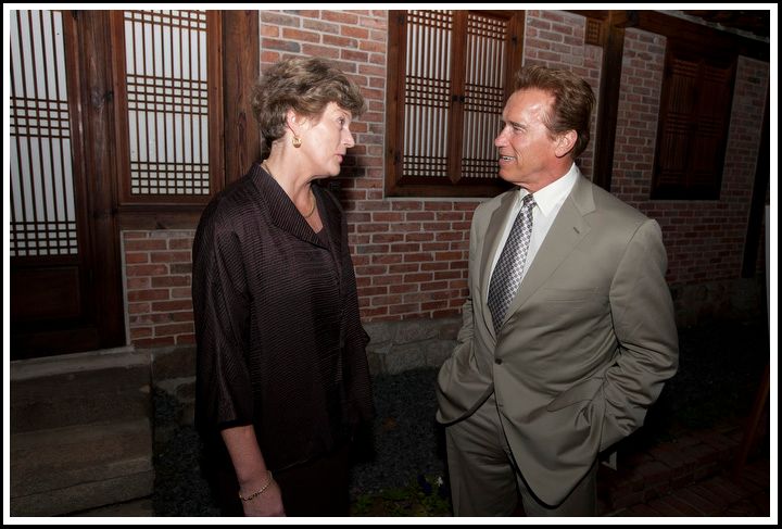 A woman and a man in a gray suit talk outside a brick building.