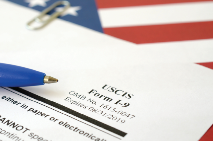 Close-up of USCIS Form I-9 beside a blue pen and an American flag.