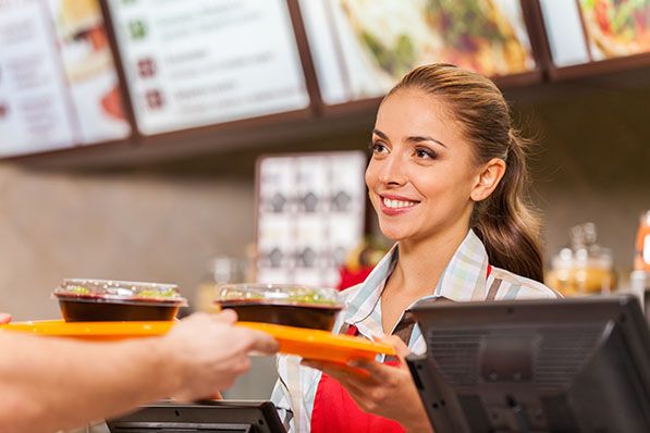 A restaurant worker hands a tray with drinks to a customer across the counter.
