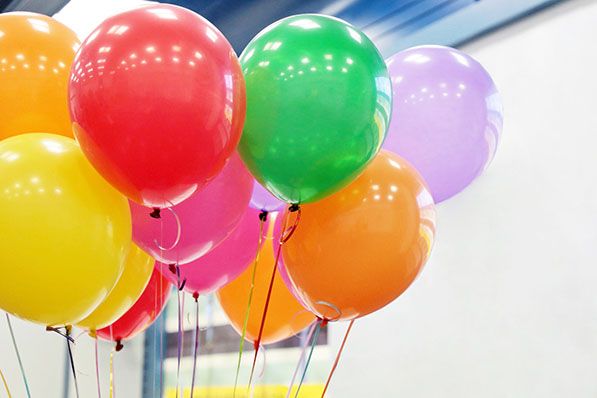 A bunch of red, yellow, green, purple, orange and pink balloons indoors.