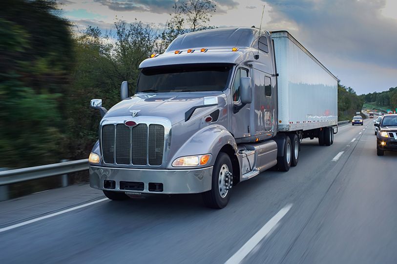 A silver tractor-trailer travels along a multilane road beside other vehicles.