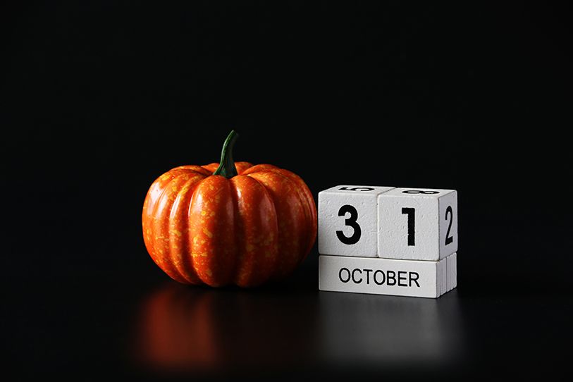 An orange pumpkin sits beside a block calendar showing October 31 on a black surface.