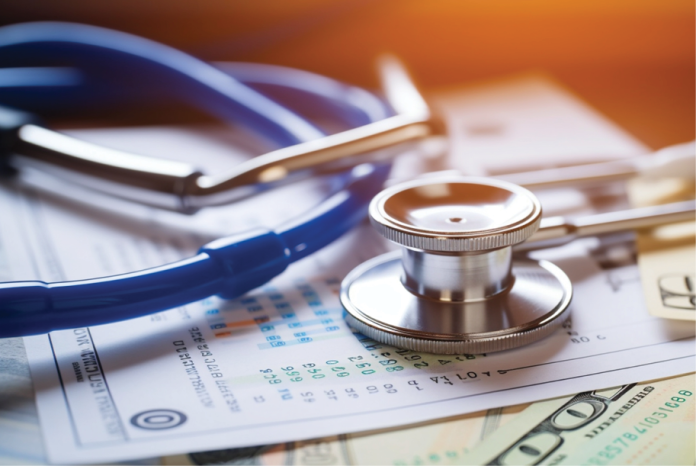 A stethoscope rests on medical paperwork and U.S. banknotes.